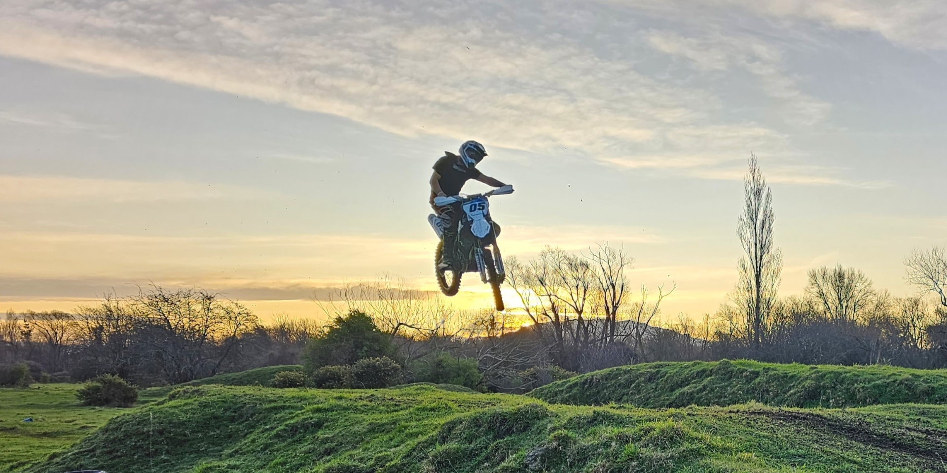 Dirt bike rider airborne against a golden sunset over a North Canterbury track